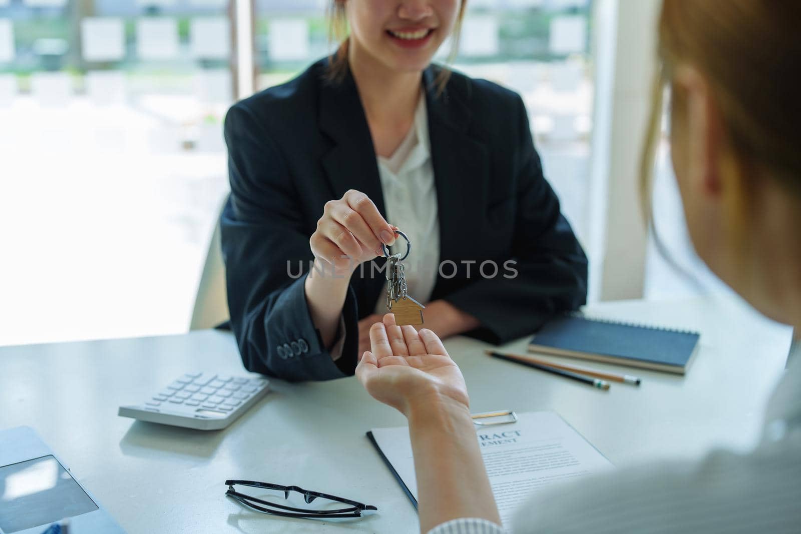 Accountant, businessman, real estate agent, Asian business woman handing keys to customers along with house after customers to sign by Manastrong