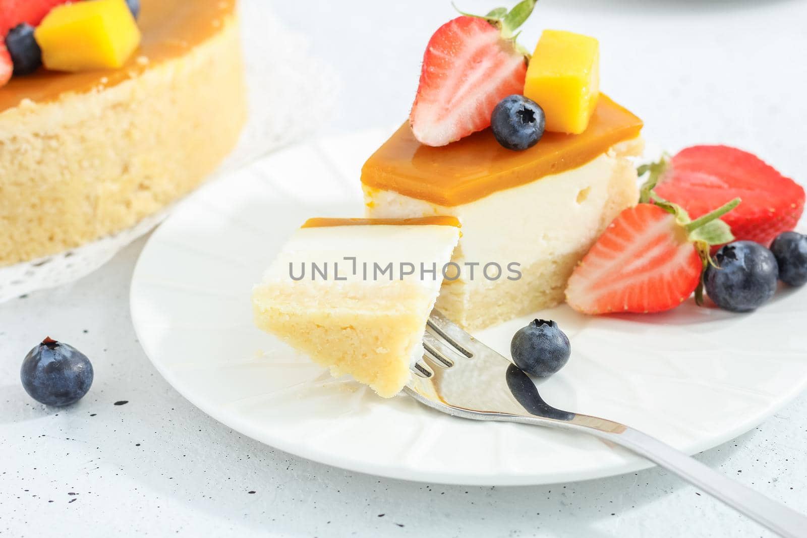 A piece of cheesecake with mango on a plate with a tea fork decorated with berries and flowers on a gray background. Healthy food.