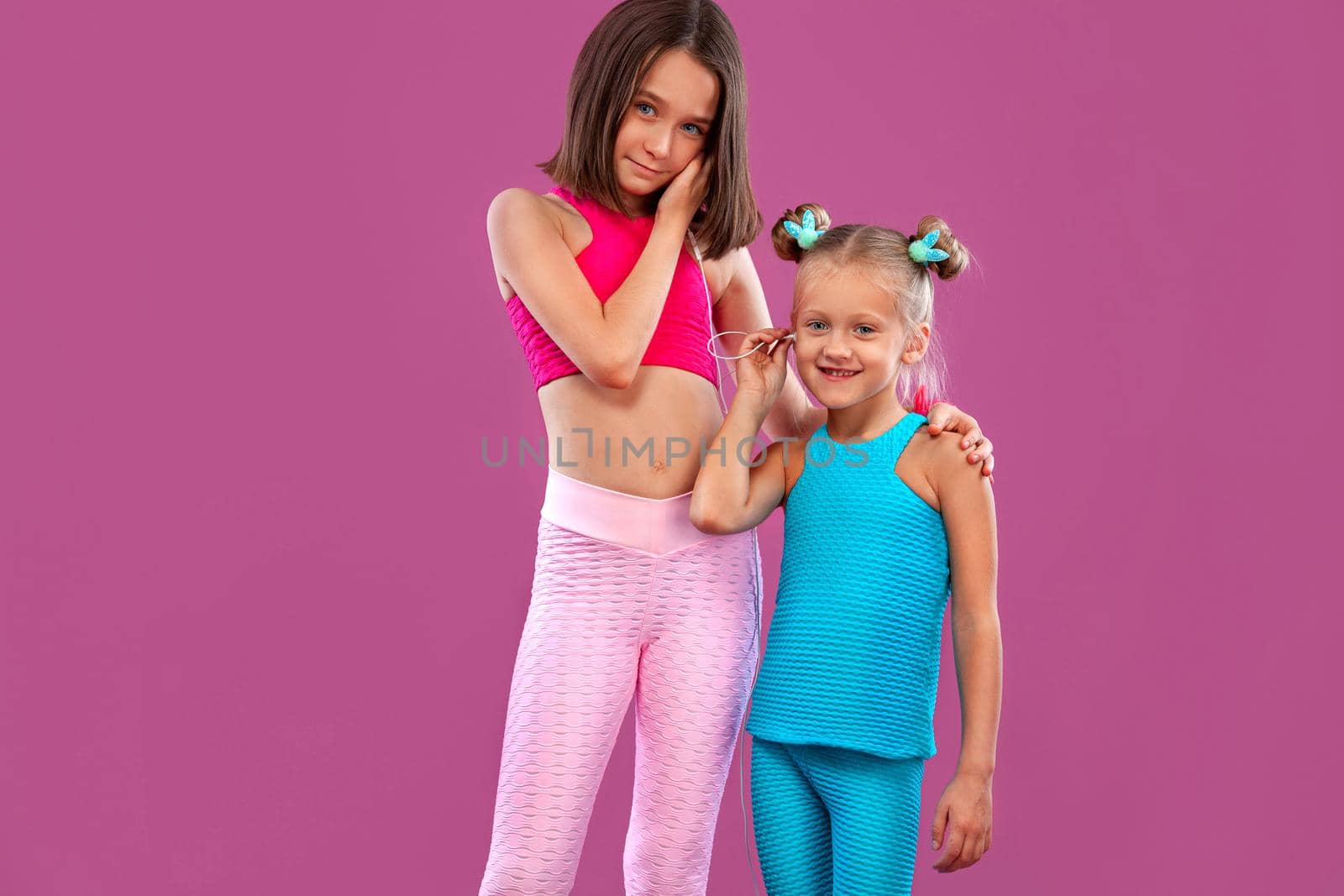 Two children girls listen to music on a pink background. Kids lifestyle concept. Sportswear for kids.