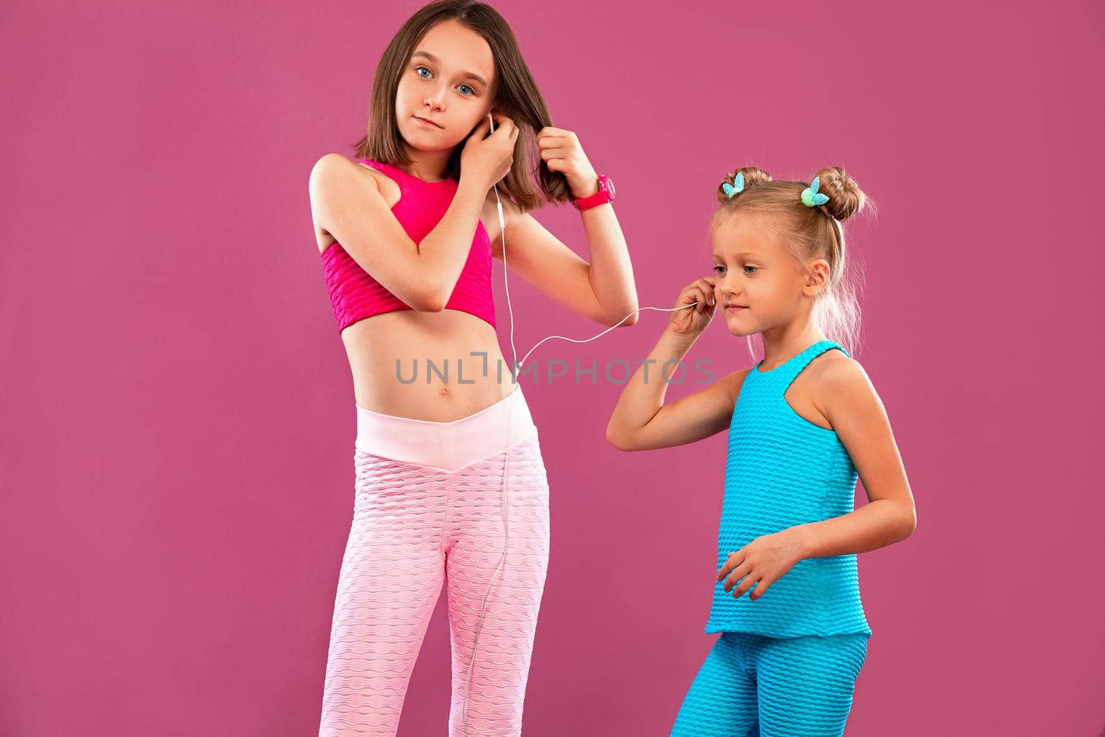 Two children girls listen to music on a pink background. Kids lifestyle concept. Sportswear for kids.