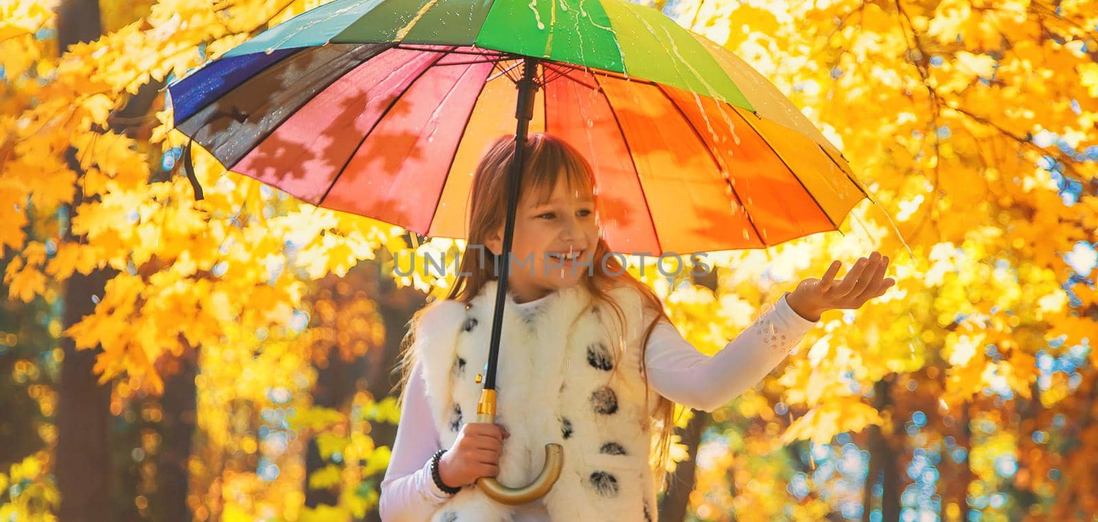 Child under an umbrella in the autumn park. Selective focus.