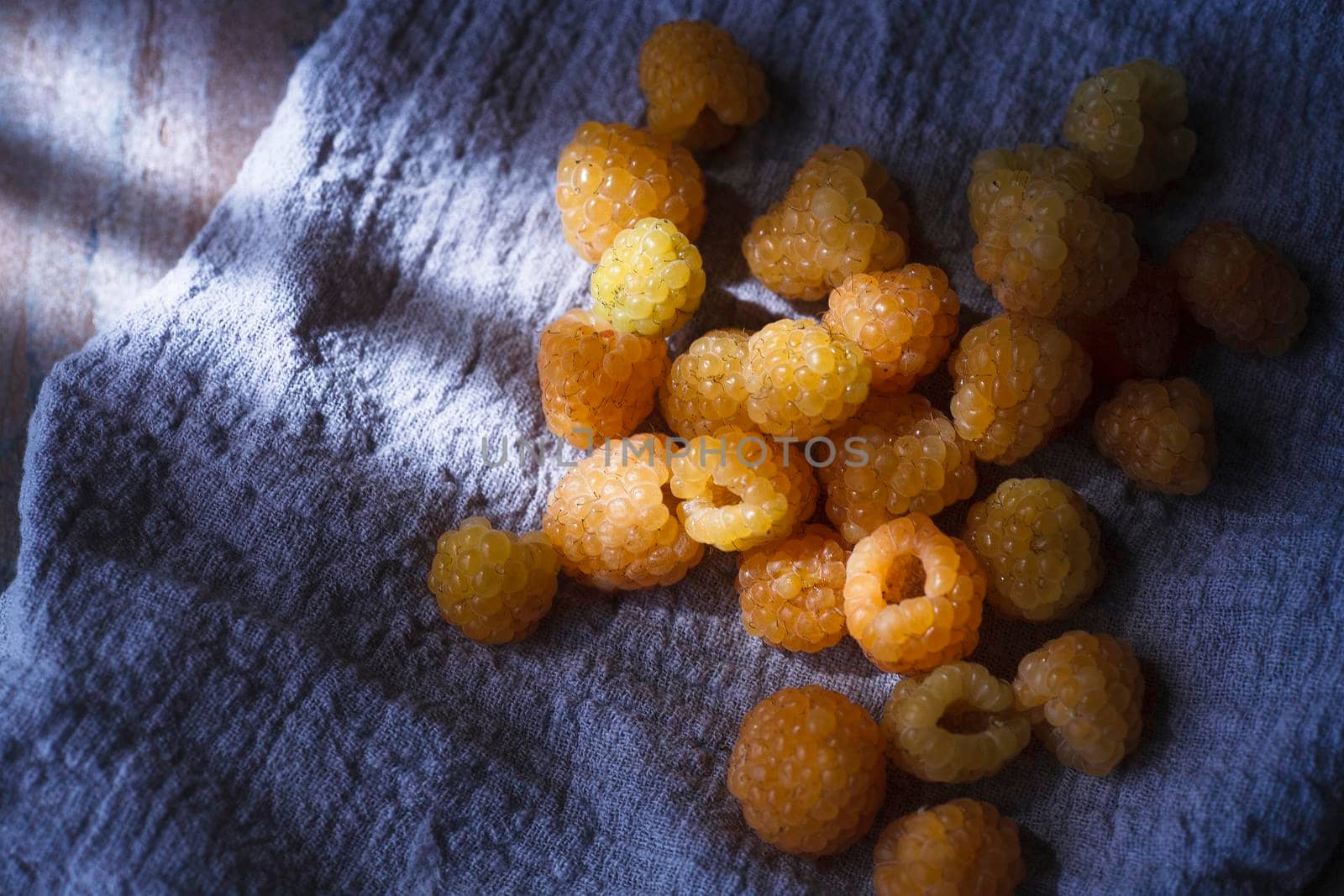 Yellow raspberry on blue cloth, extreme close up, copy space, selective focus, top view.