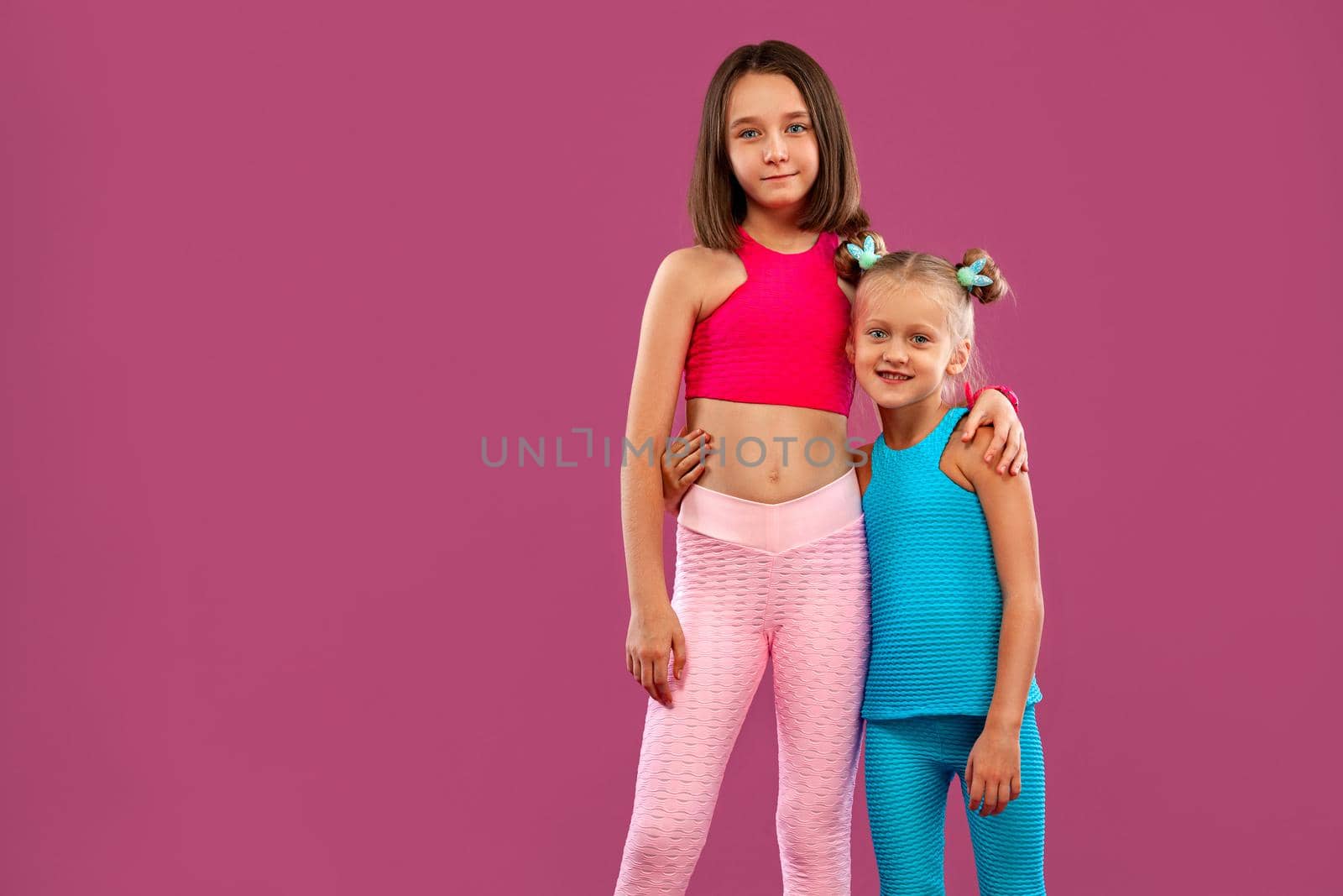 Two children girls listen to music on a pink background. Kids lifestyle concept. Sportswear for kids.