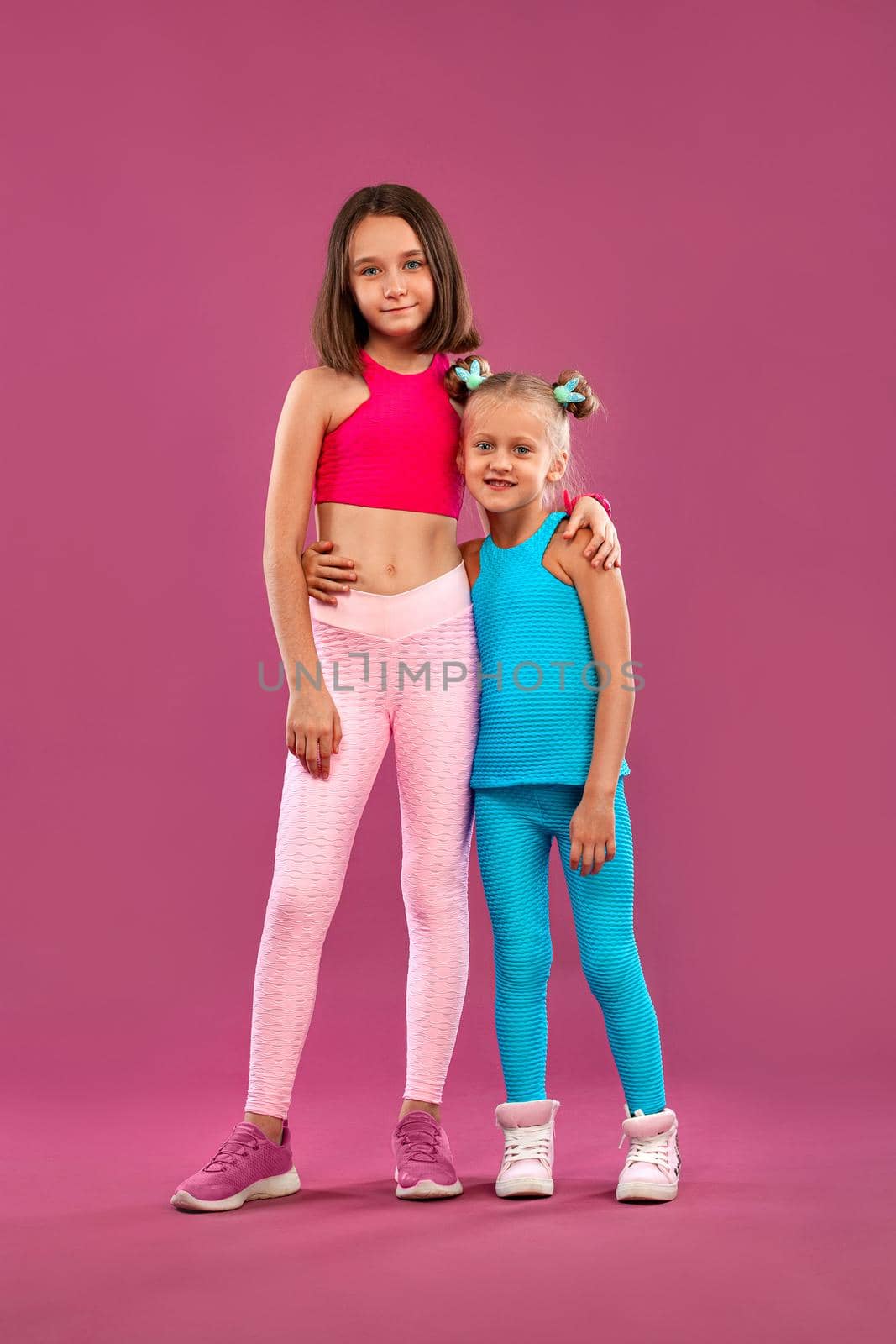 Two children girls rest after fitness exercises on a pink background. Kids lifestyle concept. by MikeOrlov