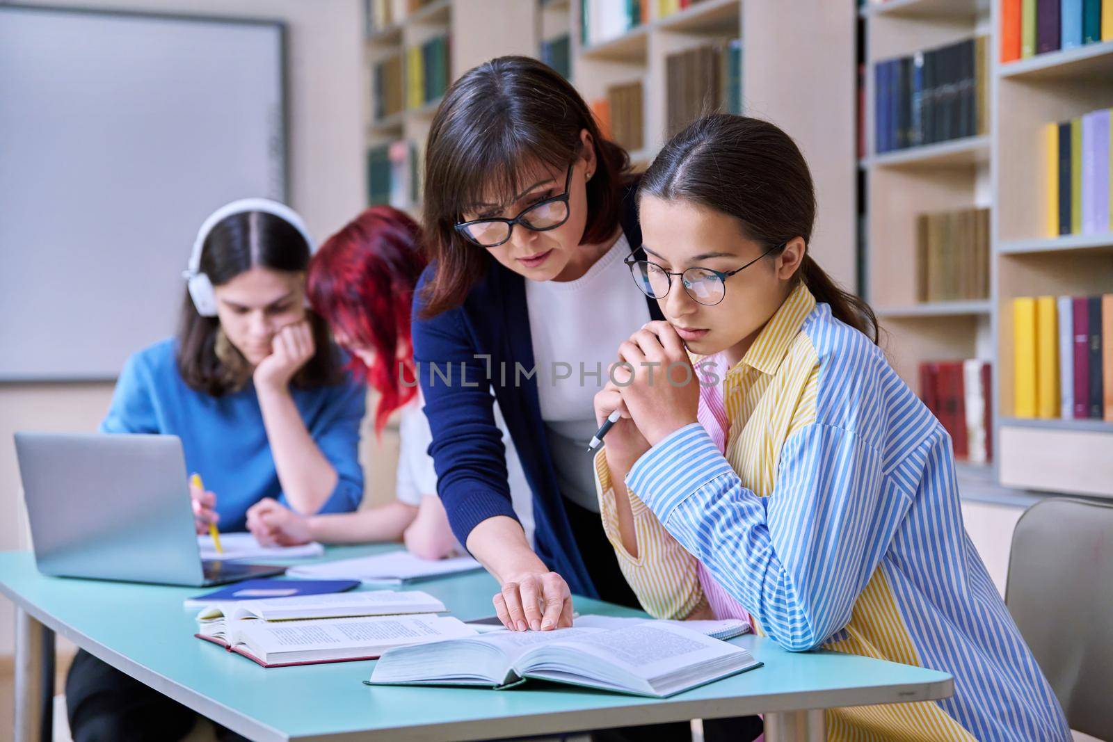 Group of teenage students and teacher study at desk in library by VH-studio