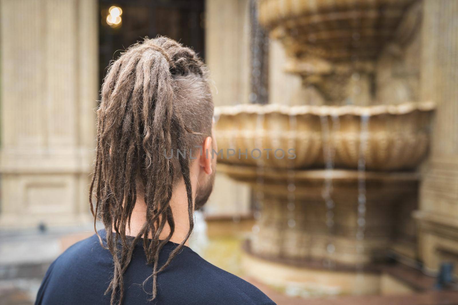 Back view of a young hipster man with dreadlocks and sidecut look at luxury restaurant.