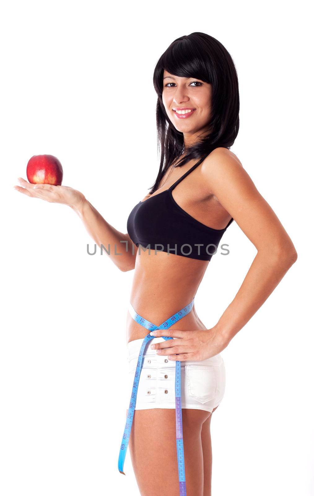 Pretty brunette girl holding apple and showing with a measuring tape around her waist how much centimeters she has already lost. Isolated on white.