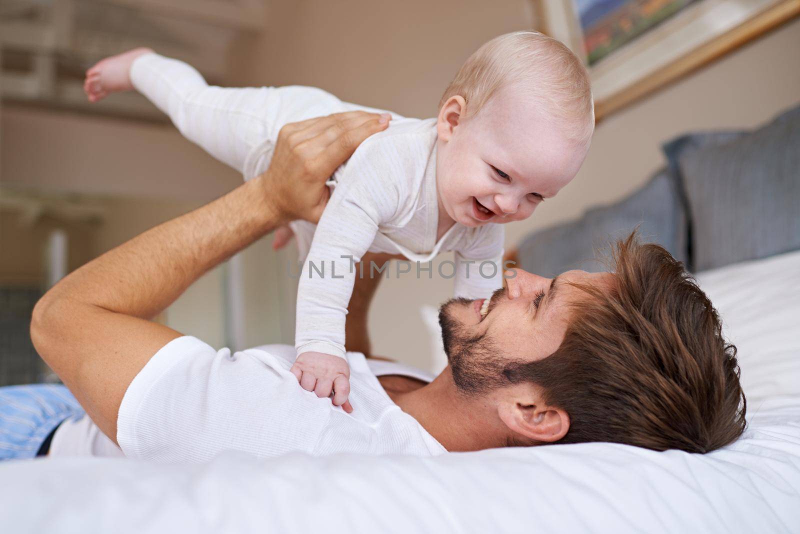 Shot of a father lying on a bed holding his baby girl up in the air.