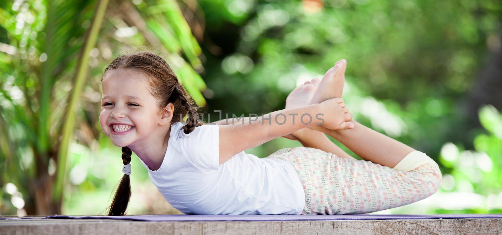 Child doing exercise on wooden platform outdoors. Healthy lifestyle. Yoga girl