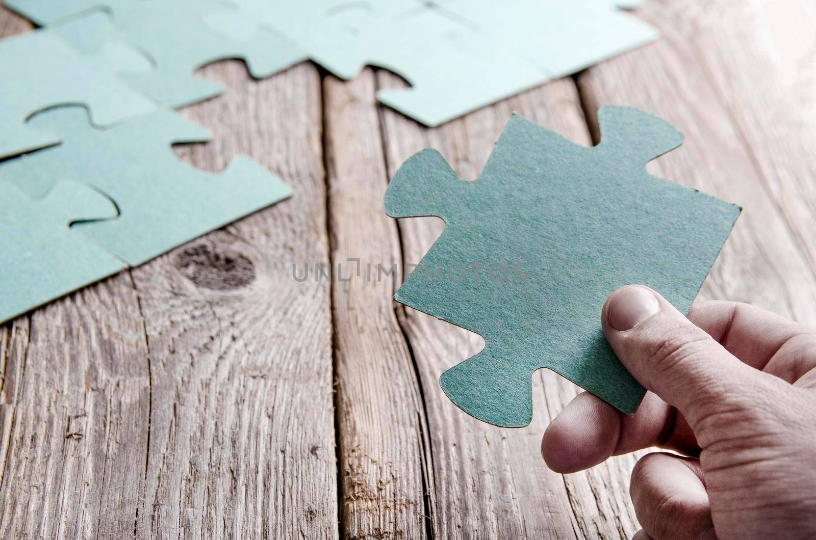 Incomplete puzzles lying on wooden rustic boards. Conceptual of innovation, solution finding and integration. Hand with puzzle piece