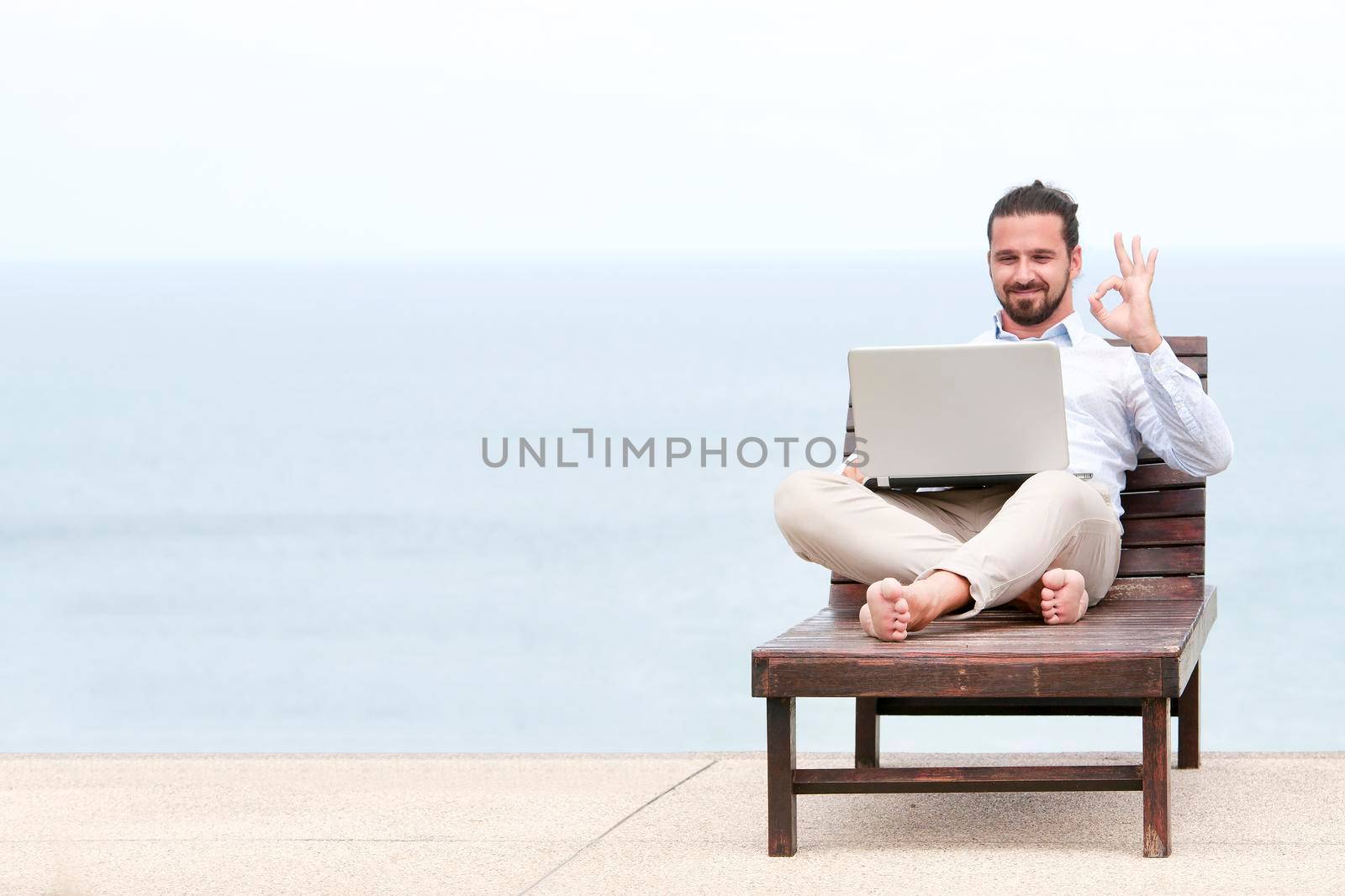 Businessman freelance on beach with laptop showing ok sign. Copy space for advertising