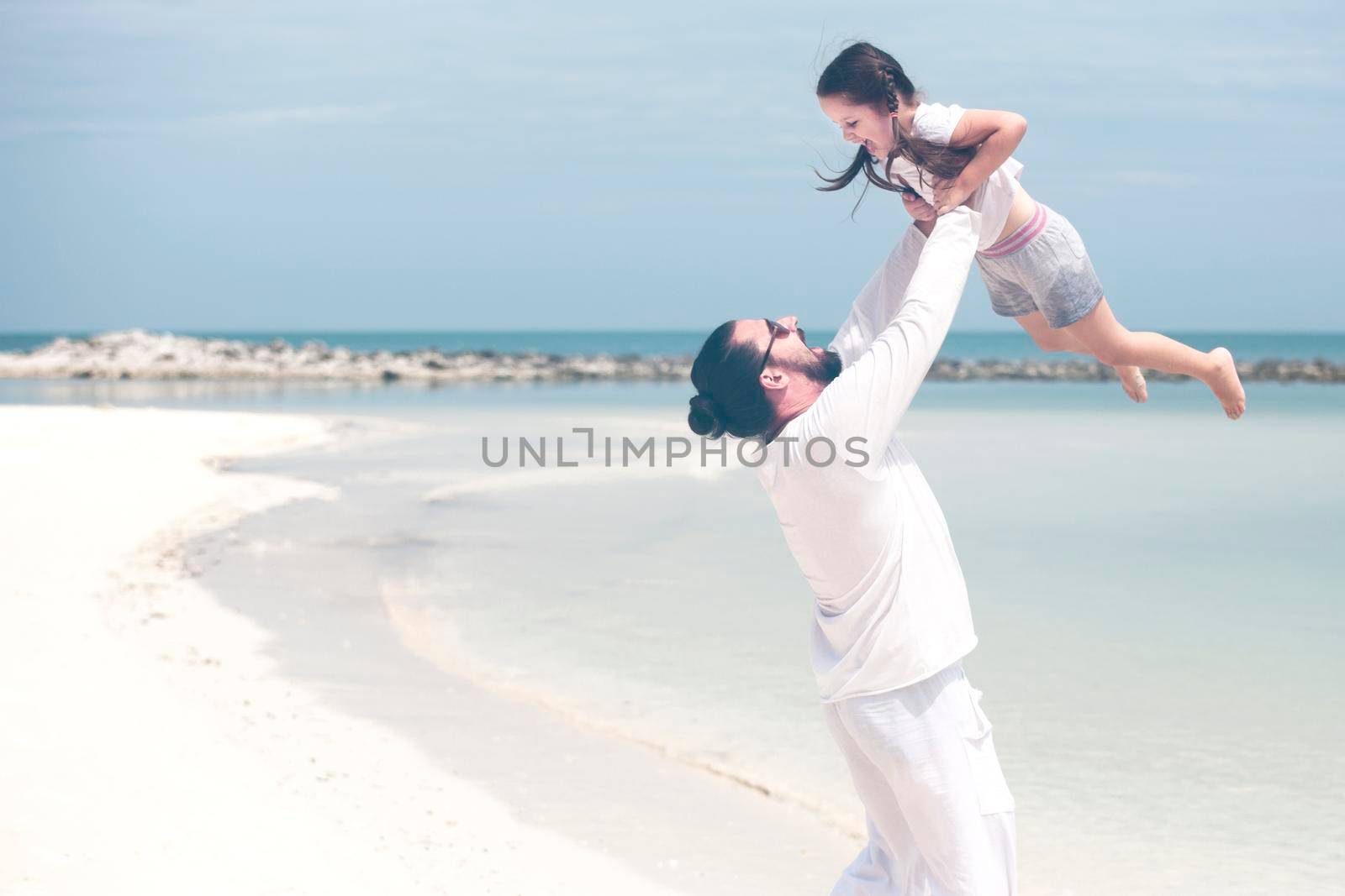 Adorable little girl holding her father hand. Father and daughter playing together at the beach. by Jyliana