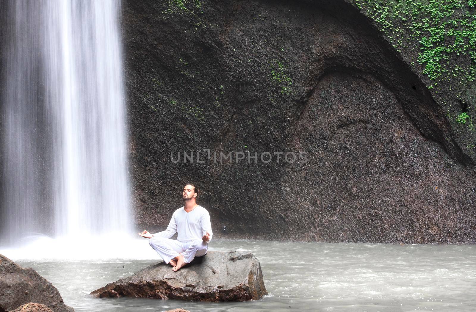 Man sitting in meditation yoga on rock at waterfall in tropical. Tibumana Waterfall