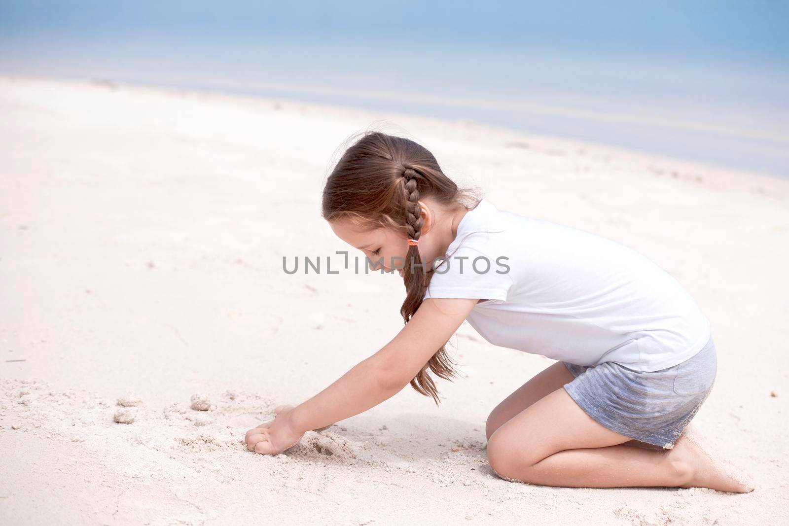 Happy child on the beach. Paradise holiday concept, girl in preschool age standing on sandy beach with blue shallow water and clean sky on background