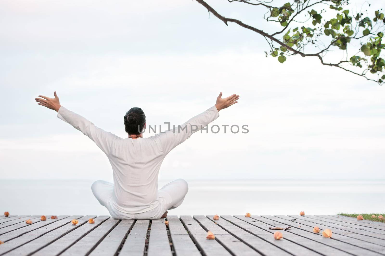 Man in white clothes meditating yoga on wooden pier by Jyliana