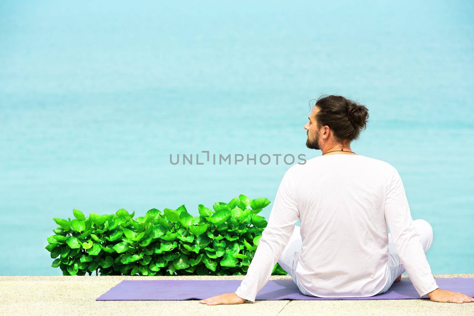 Caucasian man in white clothes meditating yoga on the sea shore pier