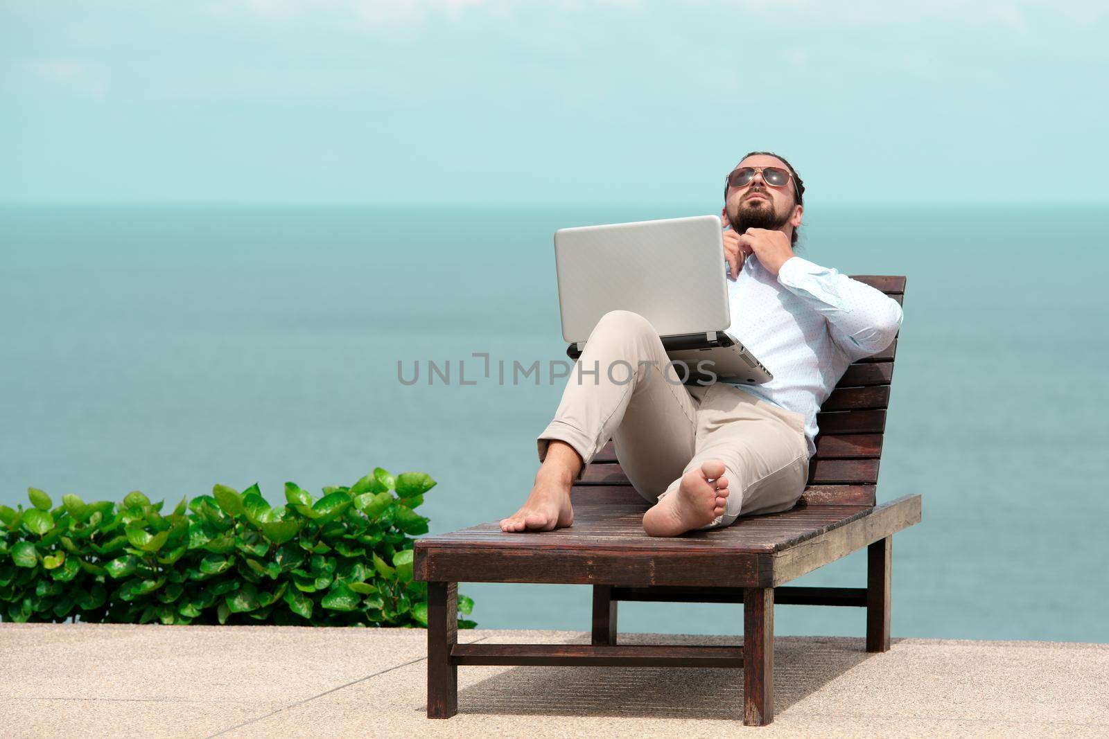 Businessman wearing a suit on deck chair typing laptop on the beach