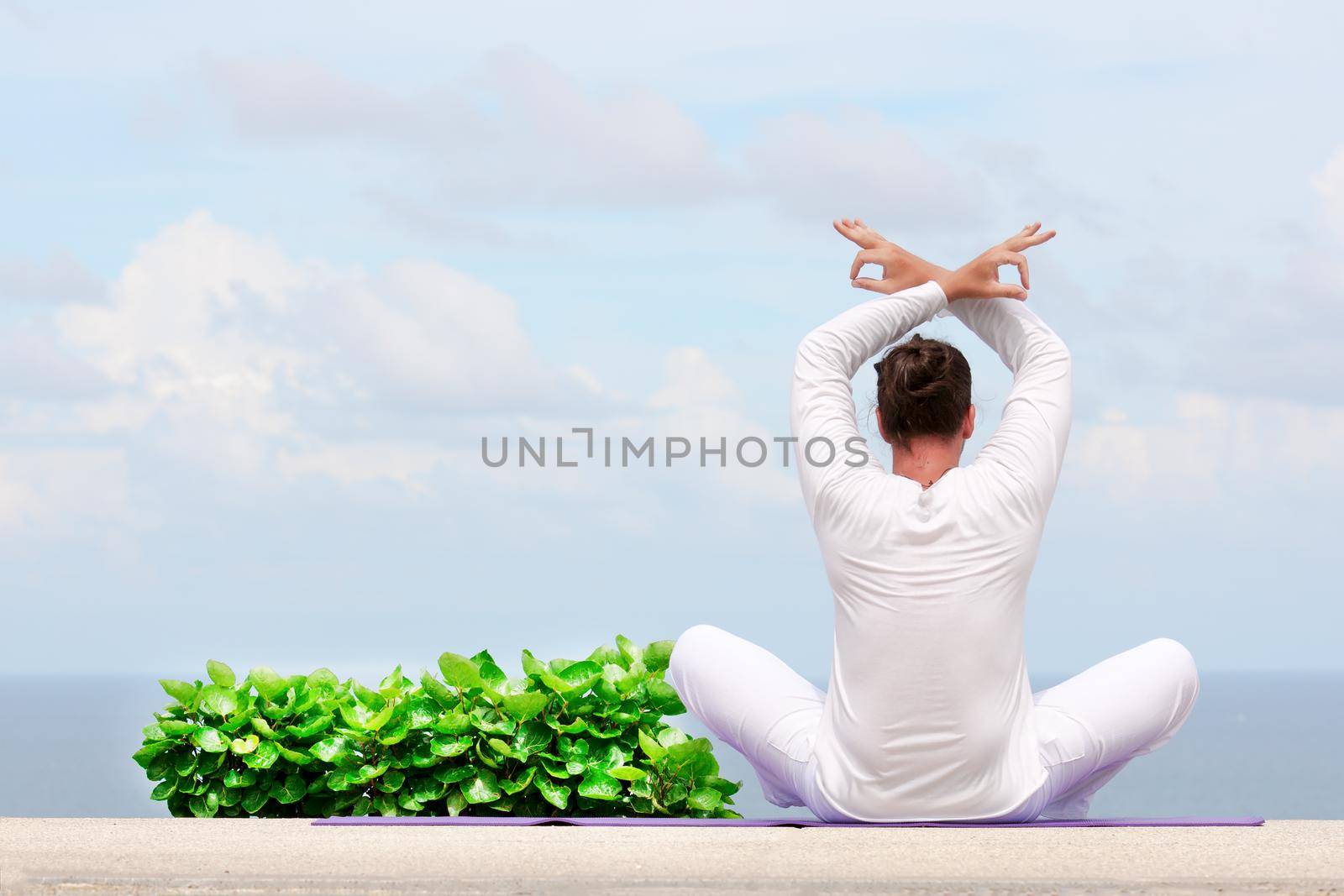 Man in white clothes meditating yoga on the sea shore by Jyliana