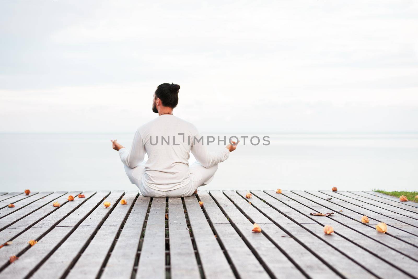 Caucasian man in white clothes meditating yoga on wooden pier platform