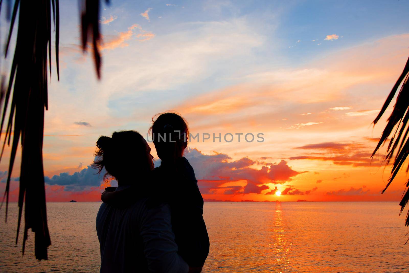 Silhouette of father and daughter on the beach at dusk. by Jyliana