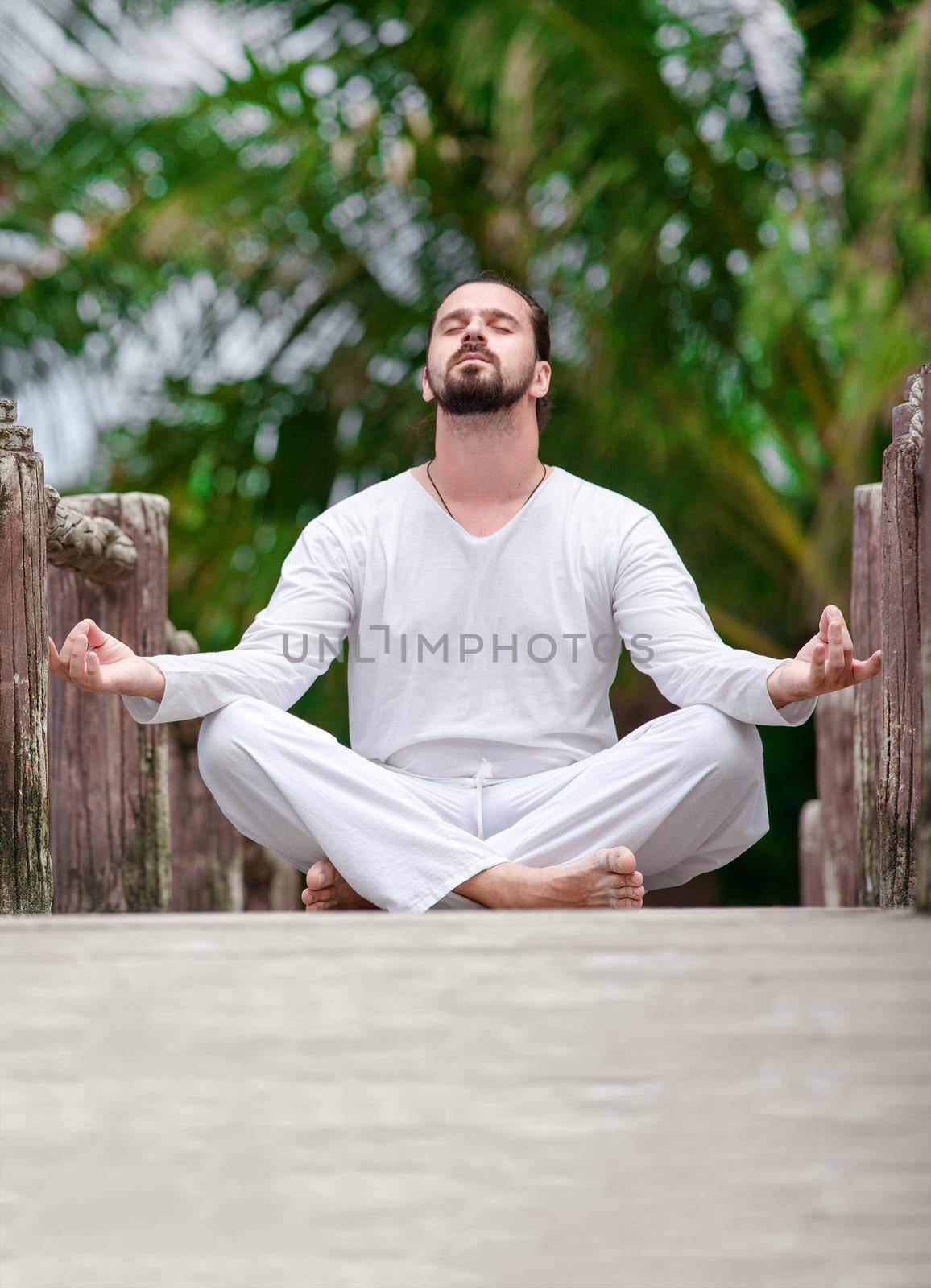 man wearingwhite doing yoga in tropic jungle bridge