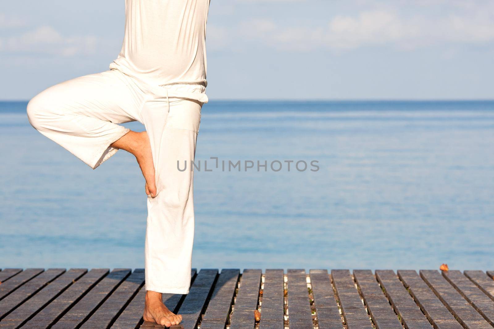 Caucasian man in white clothes meditating yoga on wooden pier