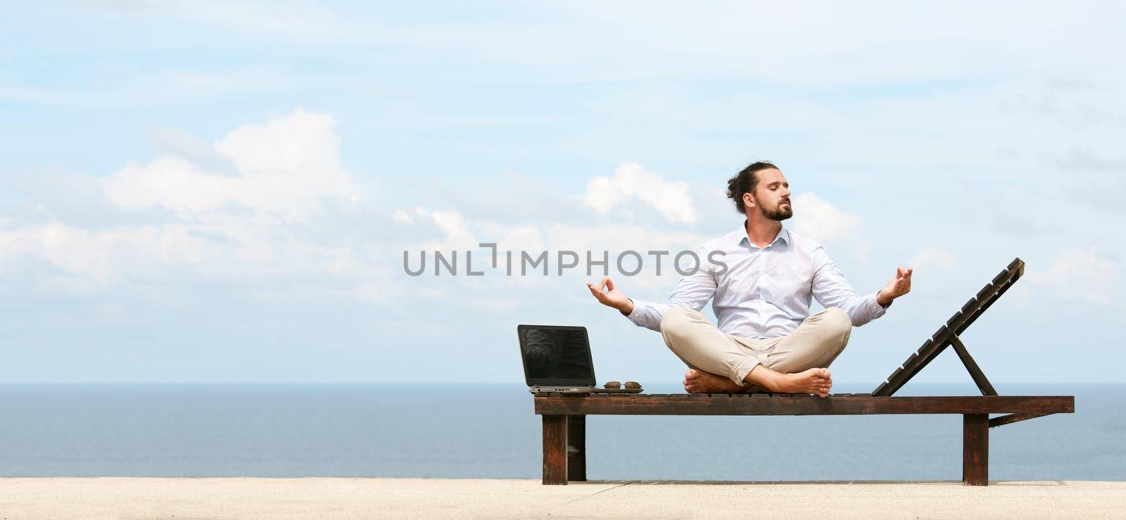 Businessman wearing a suit on deck chair doing Yoga on the beach