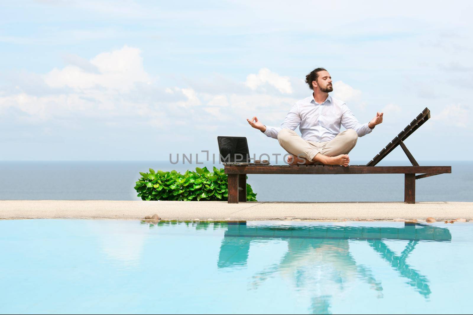 Businessman wearing a suit on deck chair doing Yoga on the beach