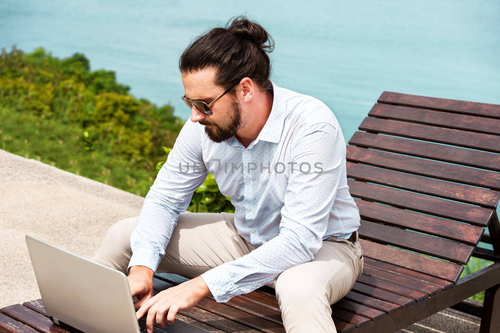 Businessman wearing a suit on deck chair typing laptop on the beach