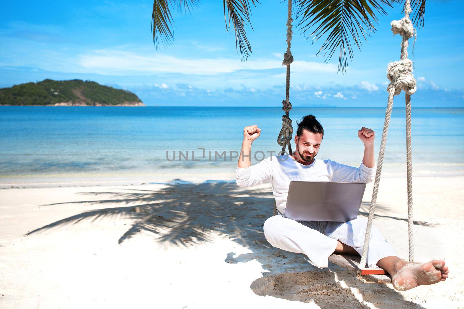 Businessman wearing white freelance sitting on beach swing with laptop