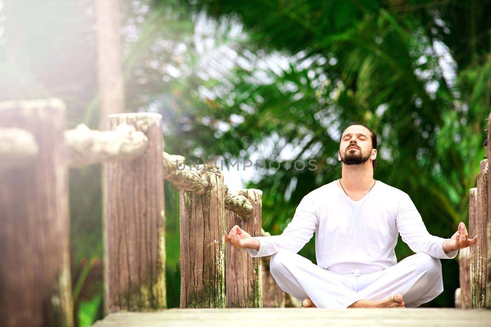 man wearing white doing yoga in tropic jungle bridge