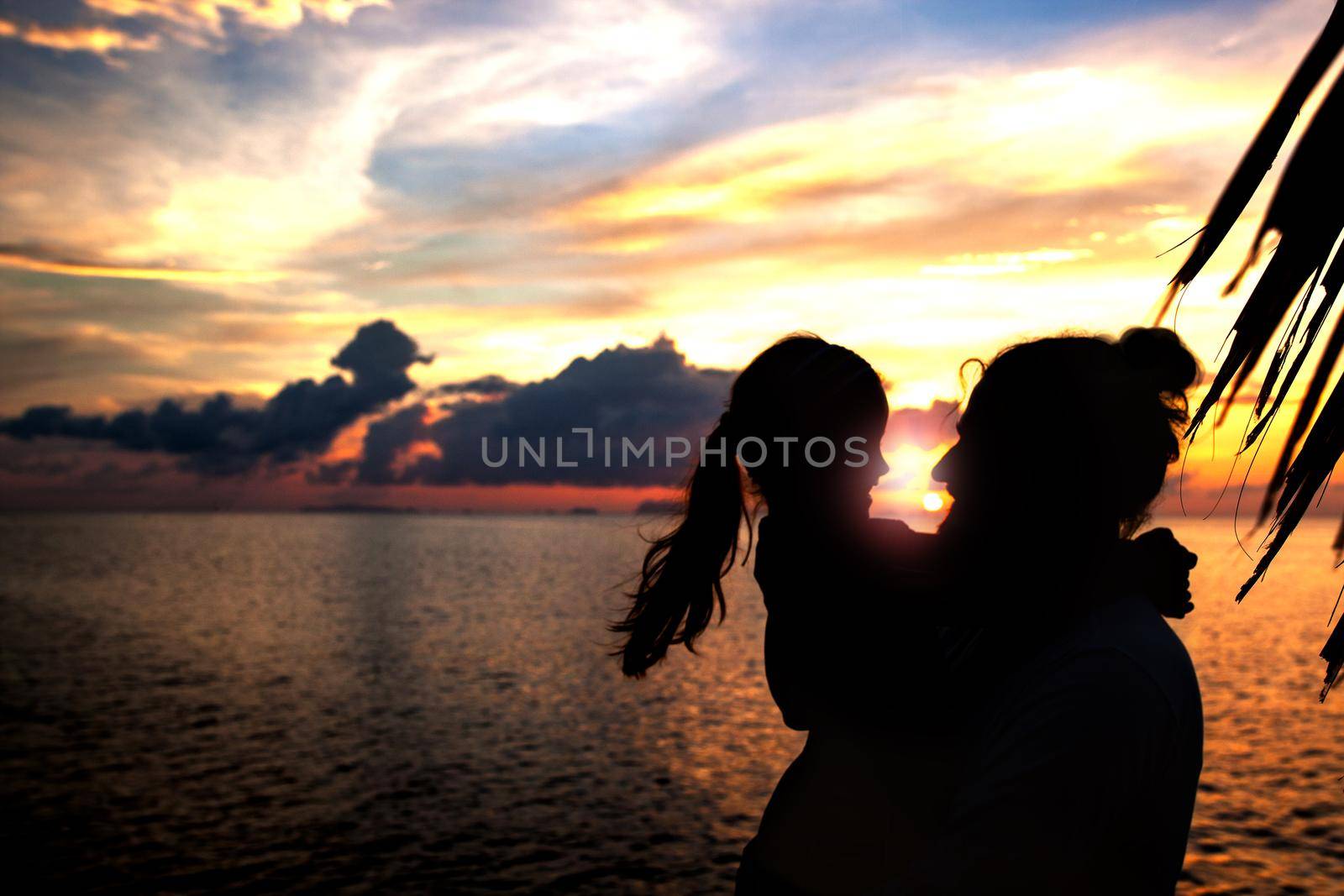 Silhouette of father and daughter on the beach at dusk. by Jyliana