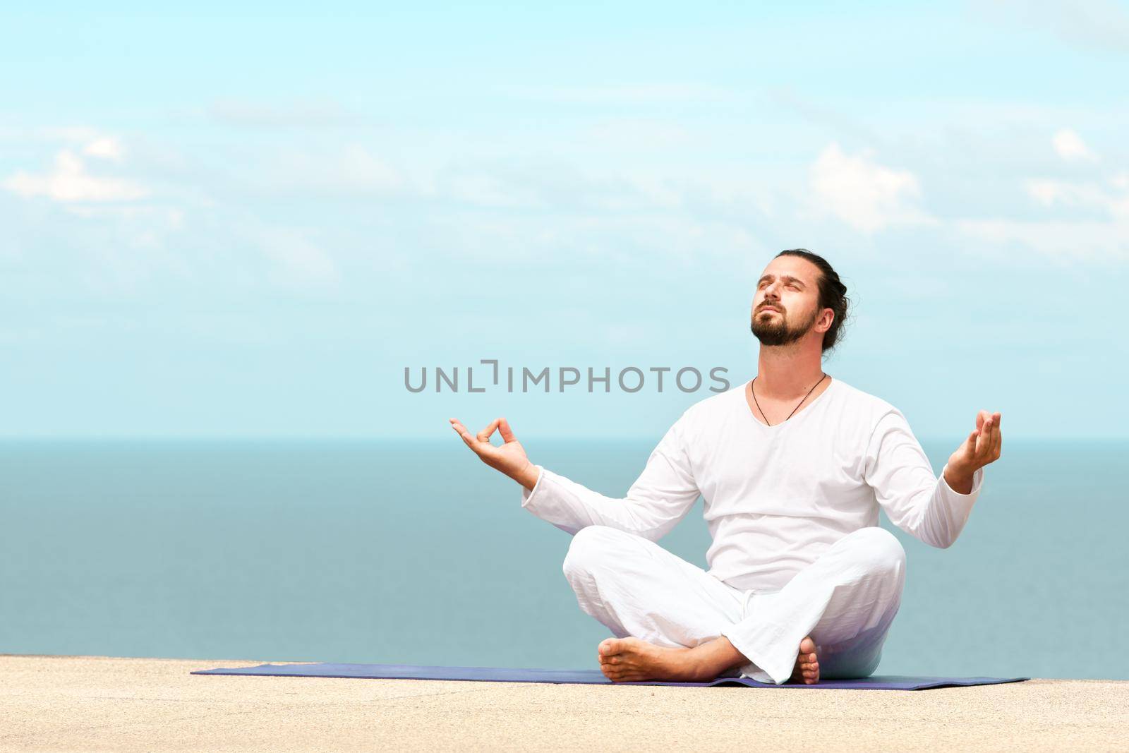 Caucasian man in white clothes meditating yoga on the sea shore pier