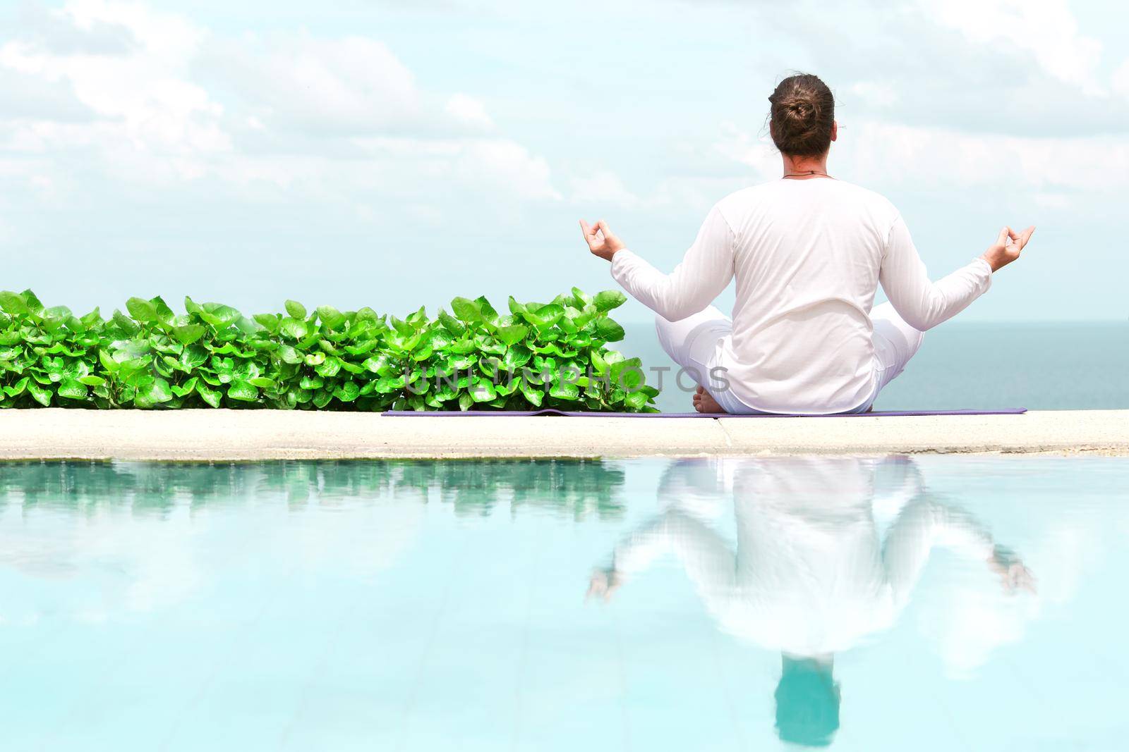 Caucasian man in white clothes meditating yoga on the sea shore pier