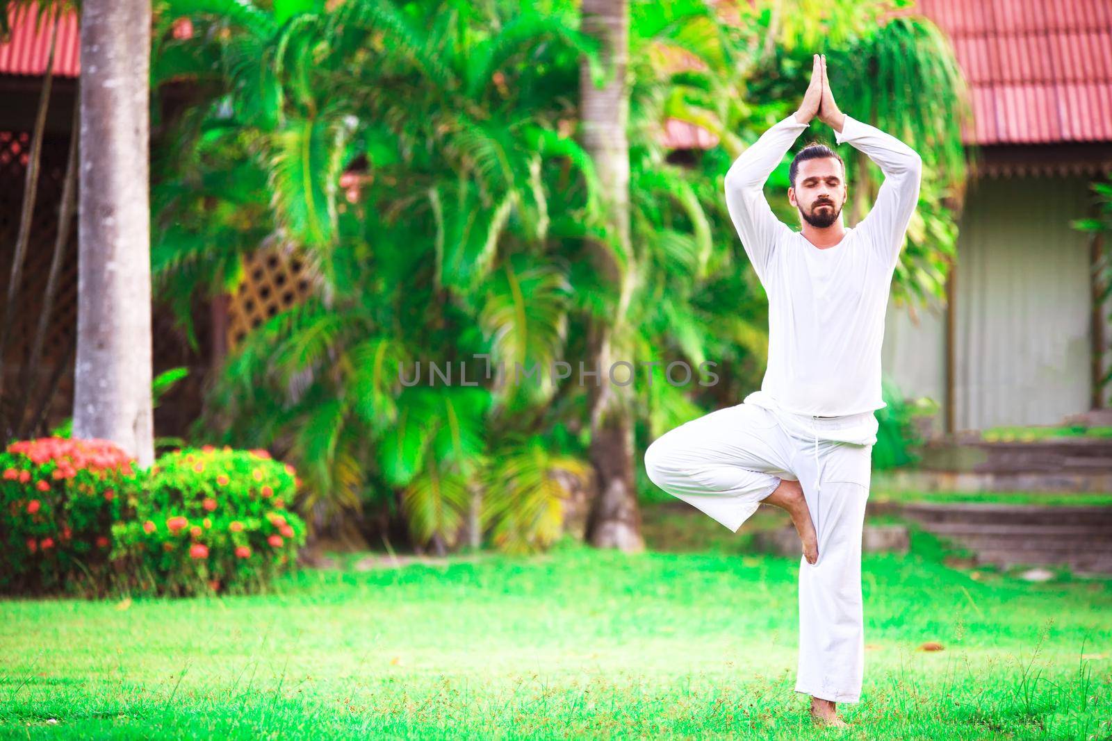 Man wearing white doing yoga in tropic jungle