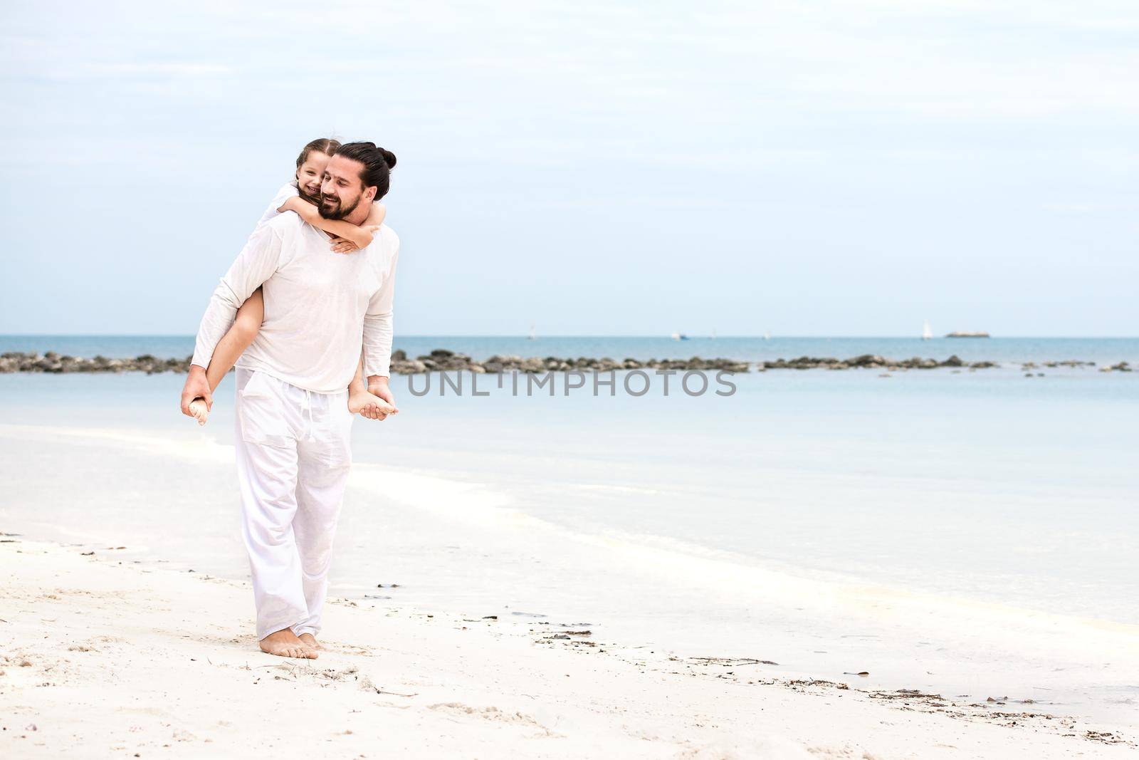 Father and daughter holding hands and walking on deserted tropical beach together happy and loving vacation