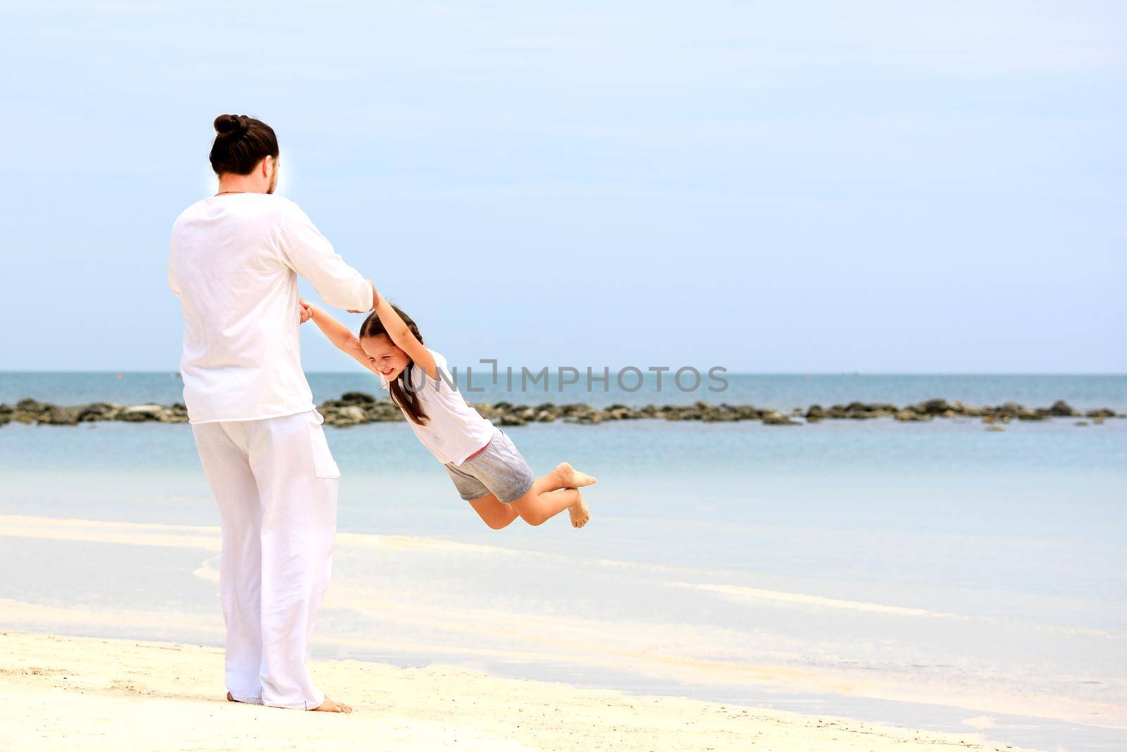 Father and daughter holding hands and walking on deserted tropical beach together happy and loving vacation