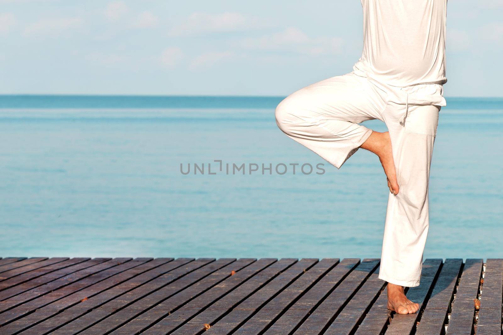 Caucasian man in white clothes meditating yoga on wooden pier