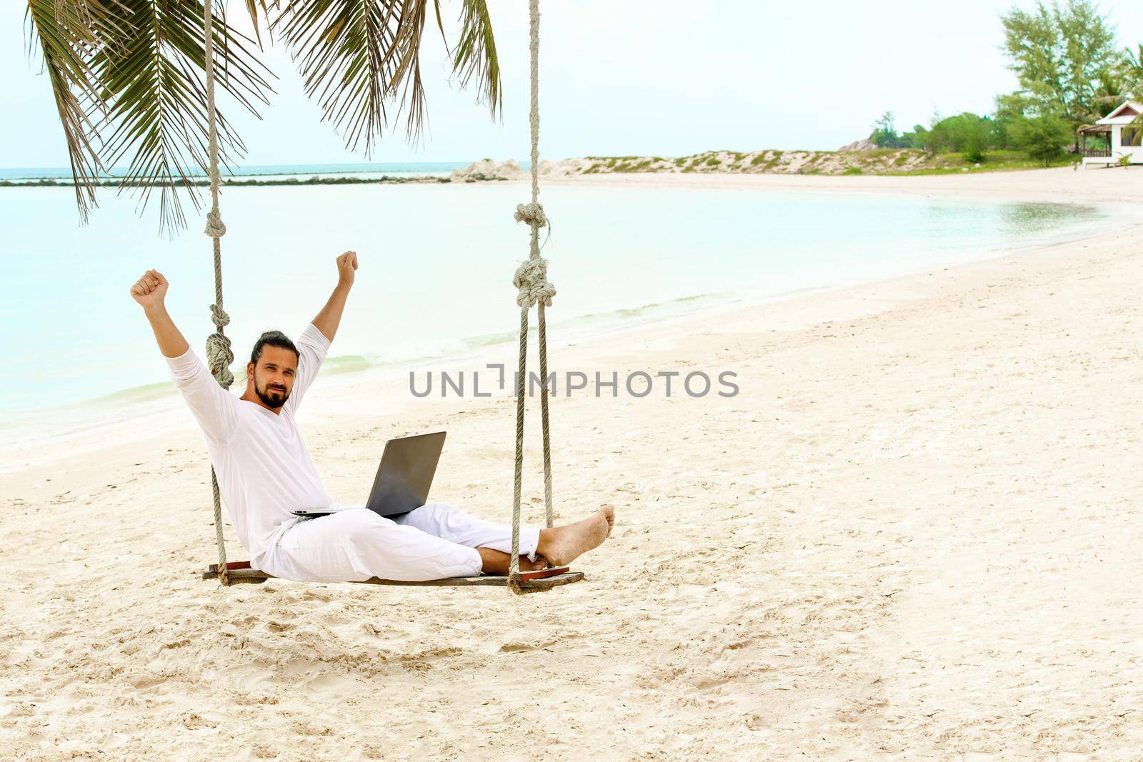 Businessman wearing white freelance sitting on beach swing with laptop