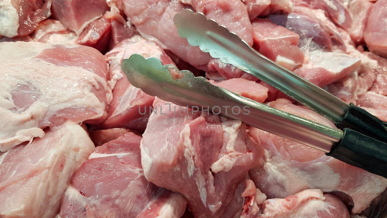 Pork is sold in a tray with steel tongs with a black handle.