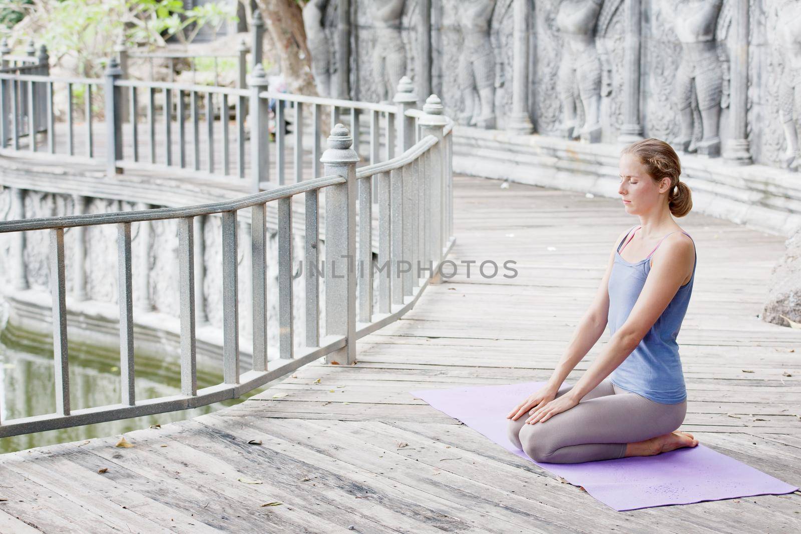 Young woman doing yoga in abandoned temple on wooden platform. Practicing. by Jyliana