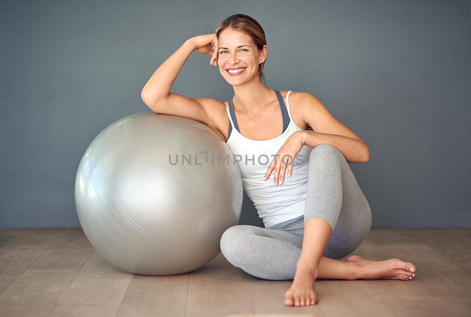 Just roll with it. Shot of a sporty young woman sitting next to her fitness ball. by YuriArcurs