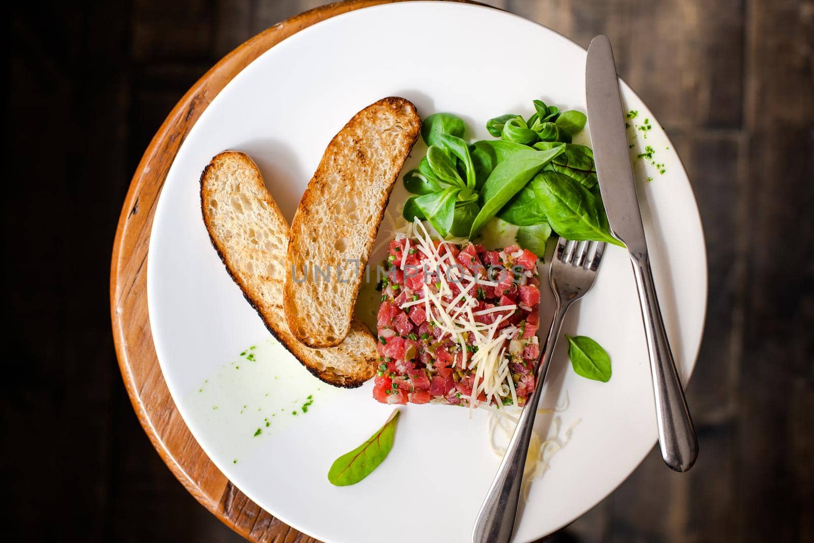 Tartare of beef with spinach on a white plate. Isolated on black or dark wooden background.