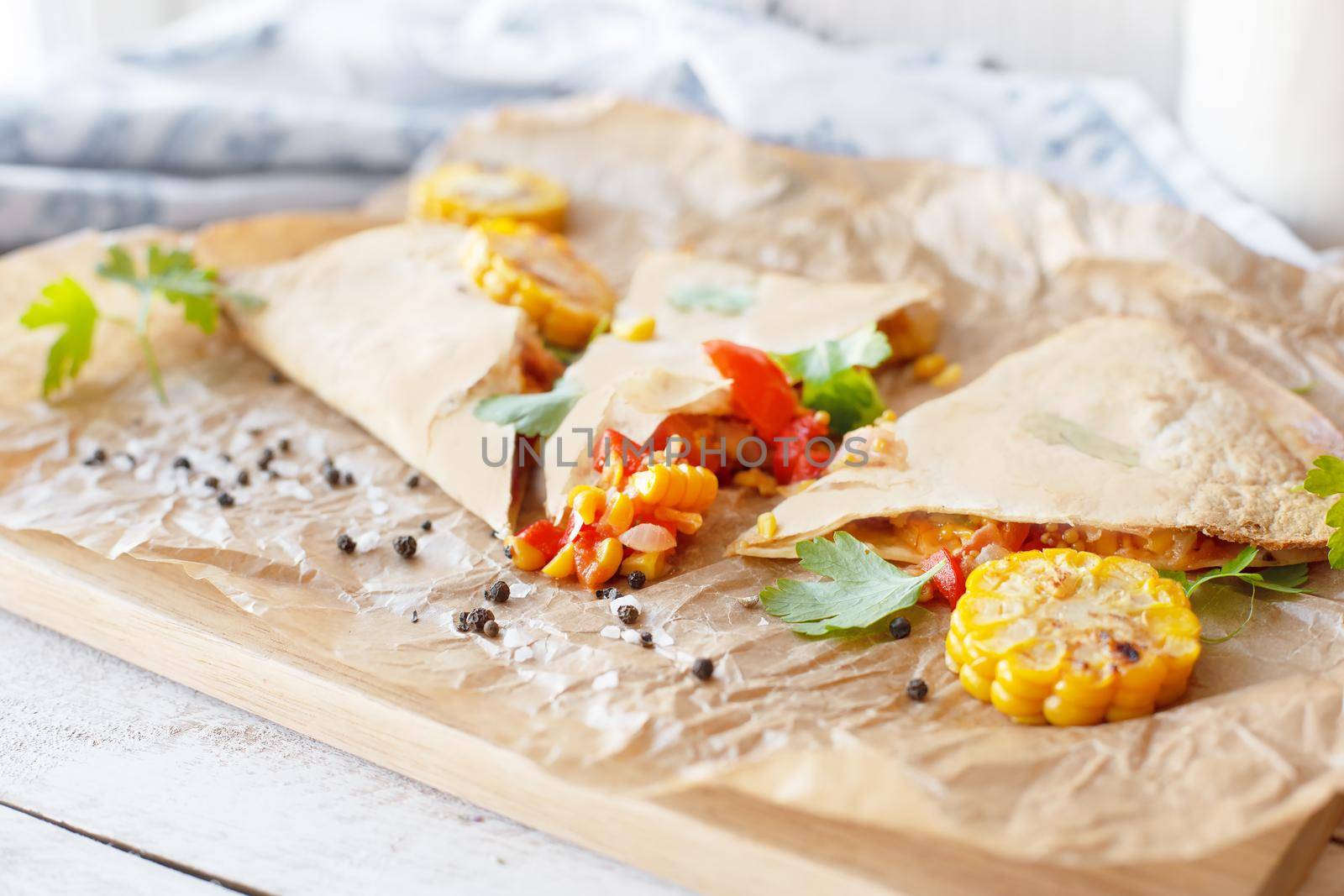 Mexican Quesadilla wrap with vegetables, corn, sweet pepper and sauces on the parchment and table. horizontal view.