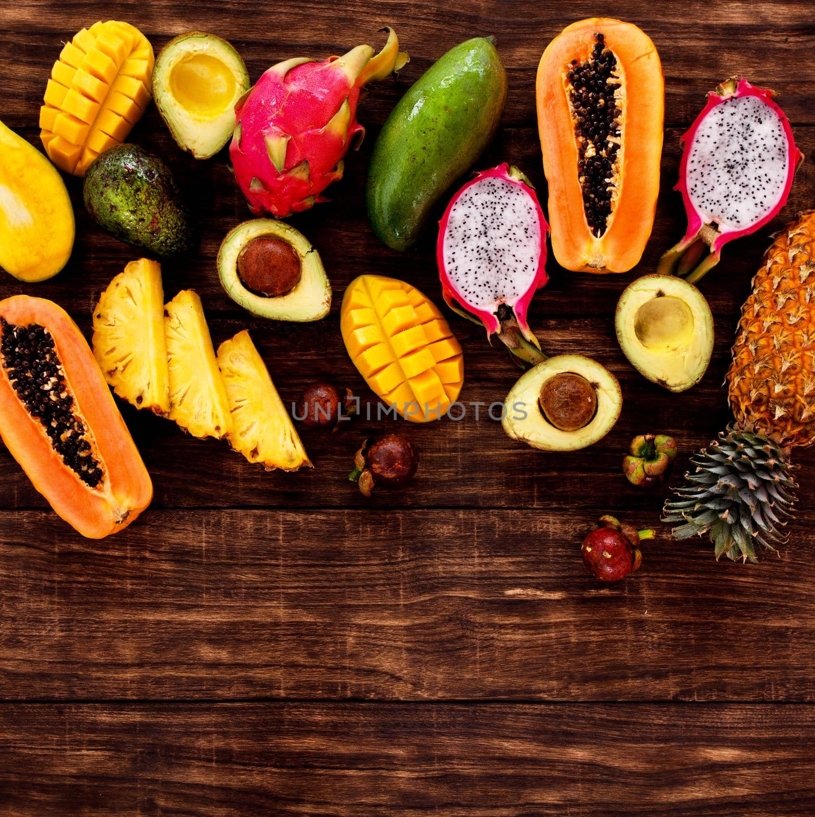 Tropical fruit on dark wooden background, top view by Jyliana