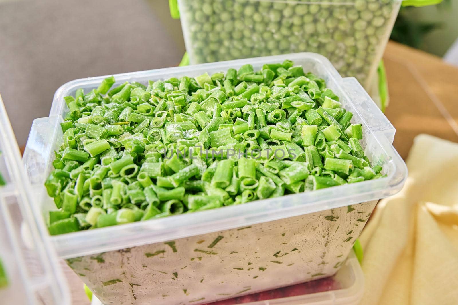 Frozen vegetables and fruits, close-up frozen in the freezer green onions, peas in plastic containers. Seasonal vegetables, food preparations for the winter