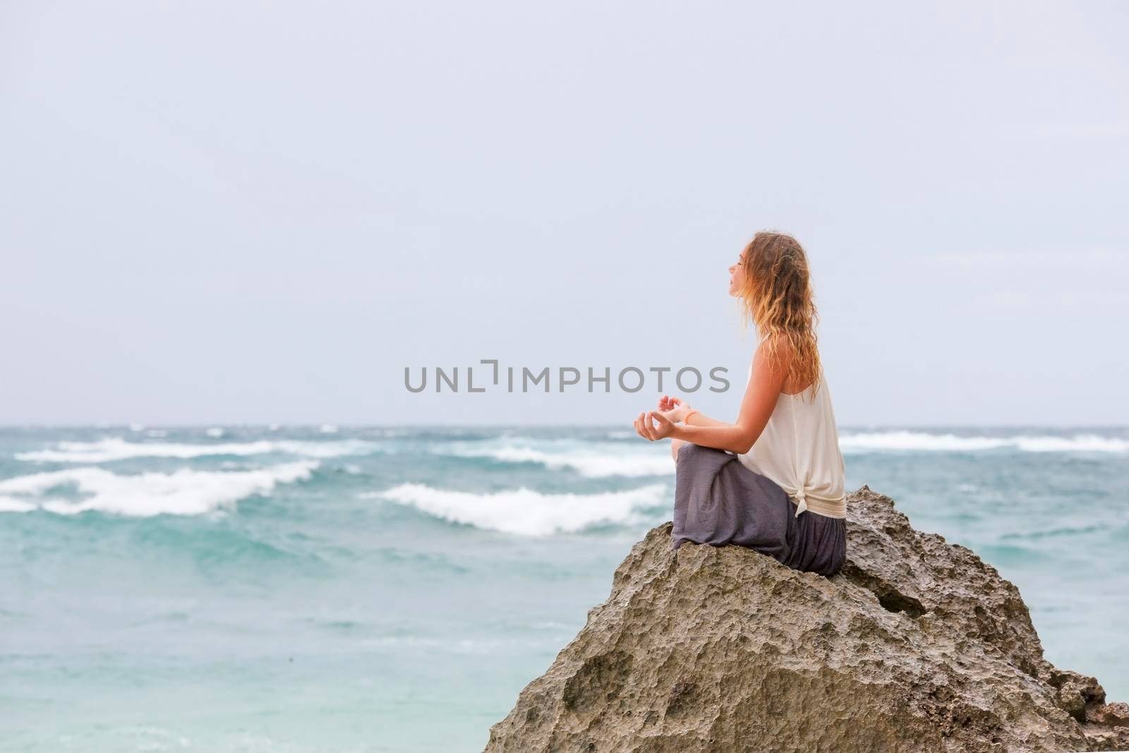 Girl sit at the seaside on the rock and meditating in yoga woman pose by Jyliana