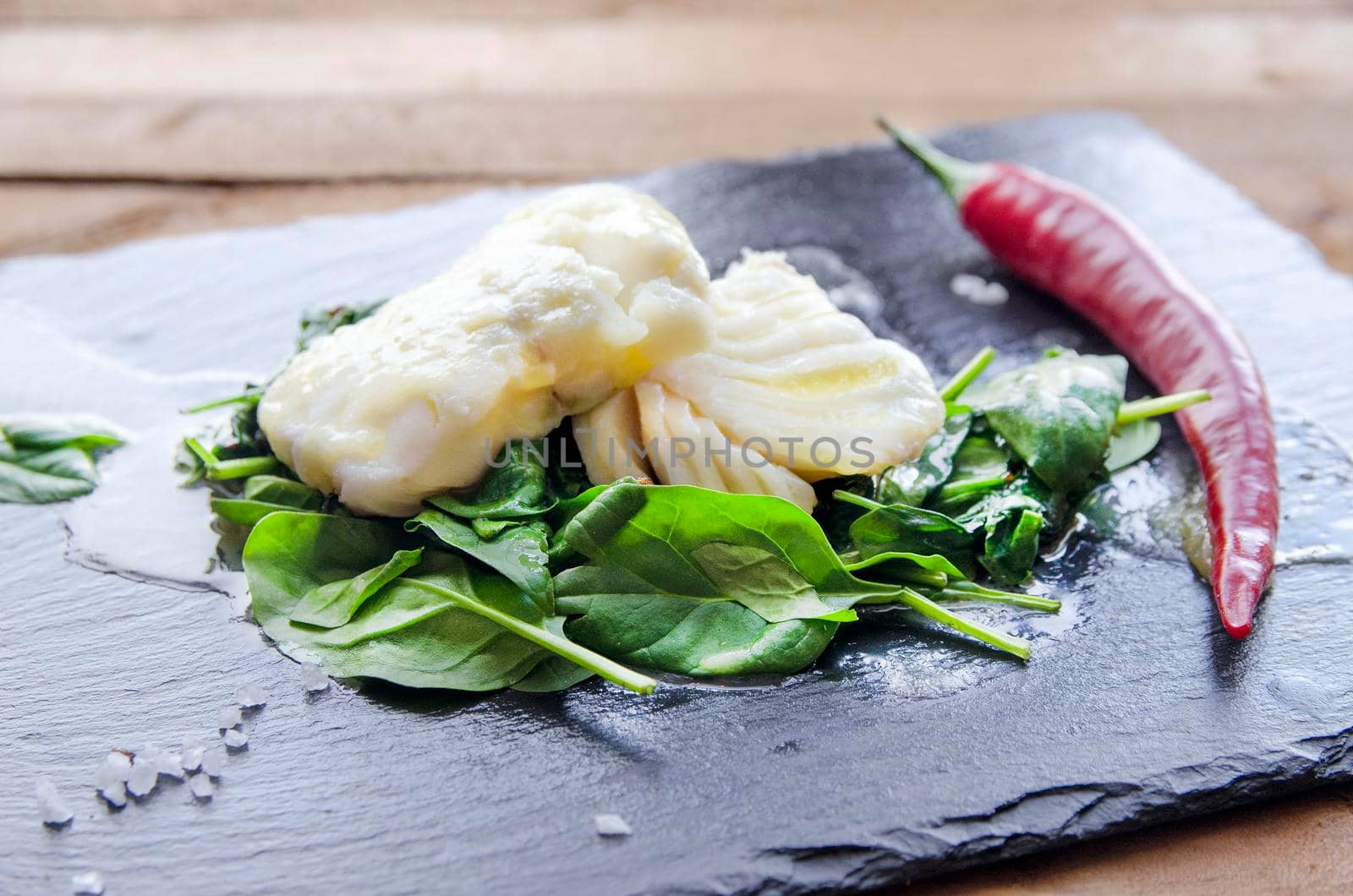 White fish fillet with herbs and chili on fried spinach. Gray background.