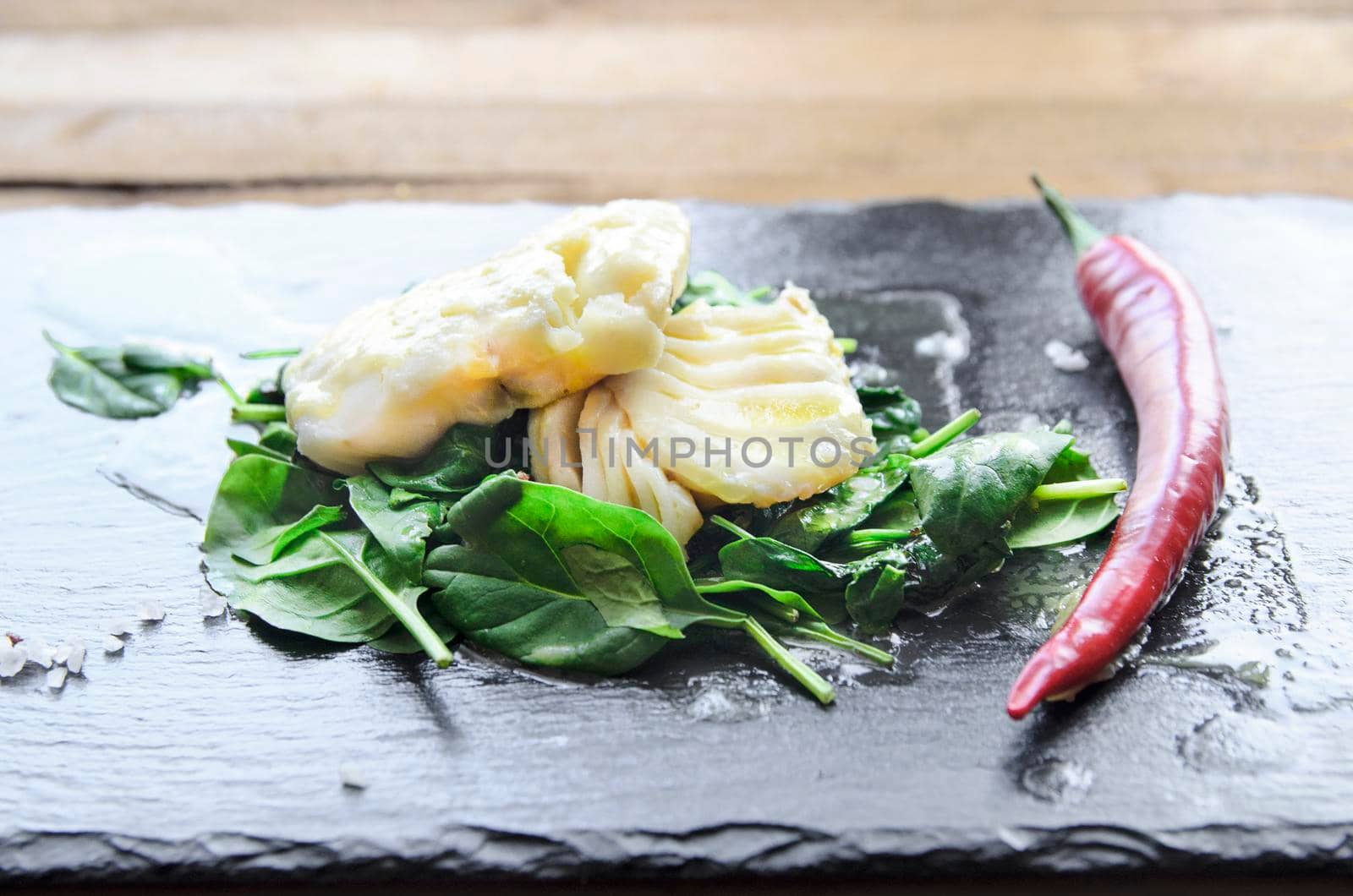 White fish fillet with chili on fried spinach. Gray background. by Jyliana