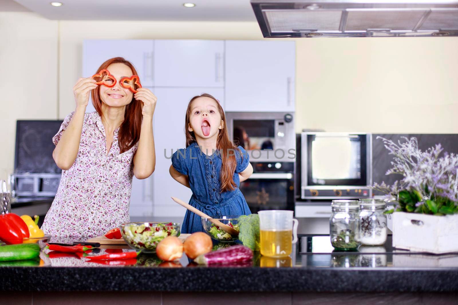 Mother and funny daughter playing in the kitchen with vegetables. Family concept